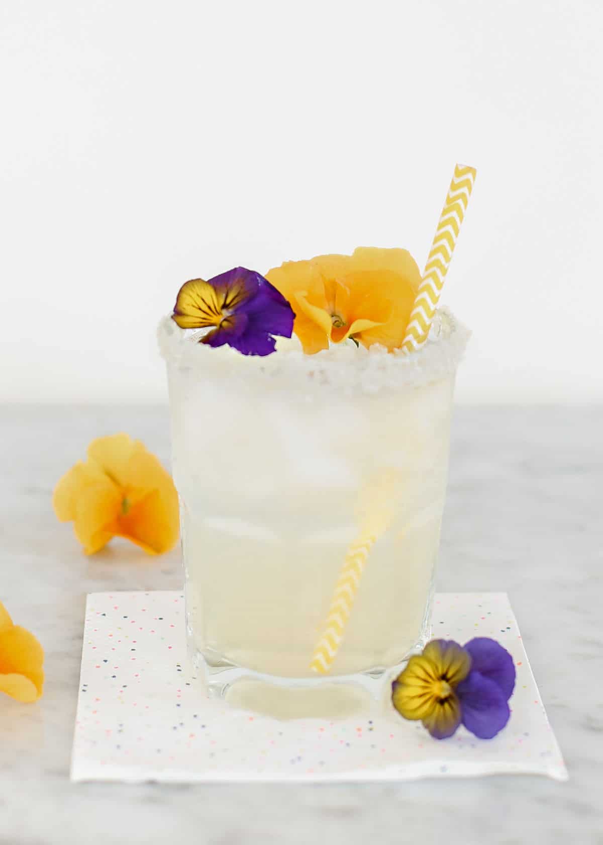 short glass with margarita drink garnished with yellow and purple flowers.