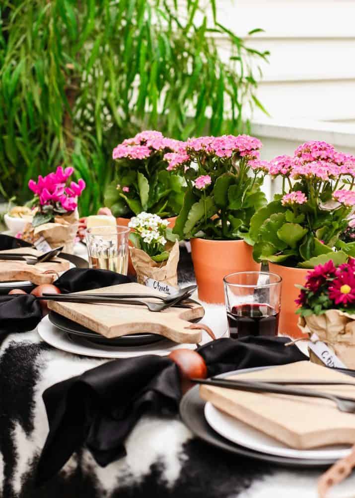 outdoor tablescape with black and white table cover, dishes, and pink potted flowers centerpiece.