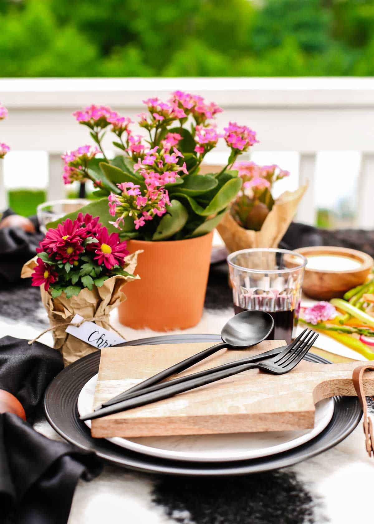 outdoor tablescape with layered black and white dishes and individual wood cutting board on top.