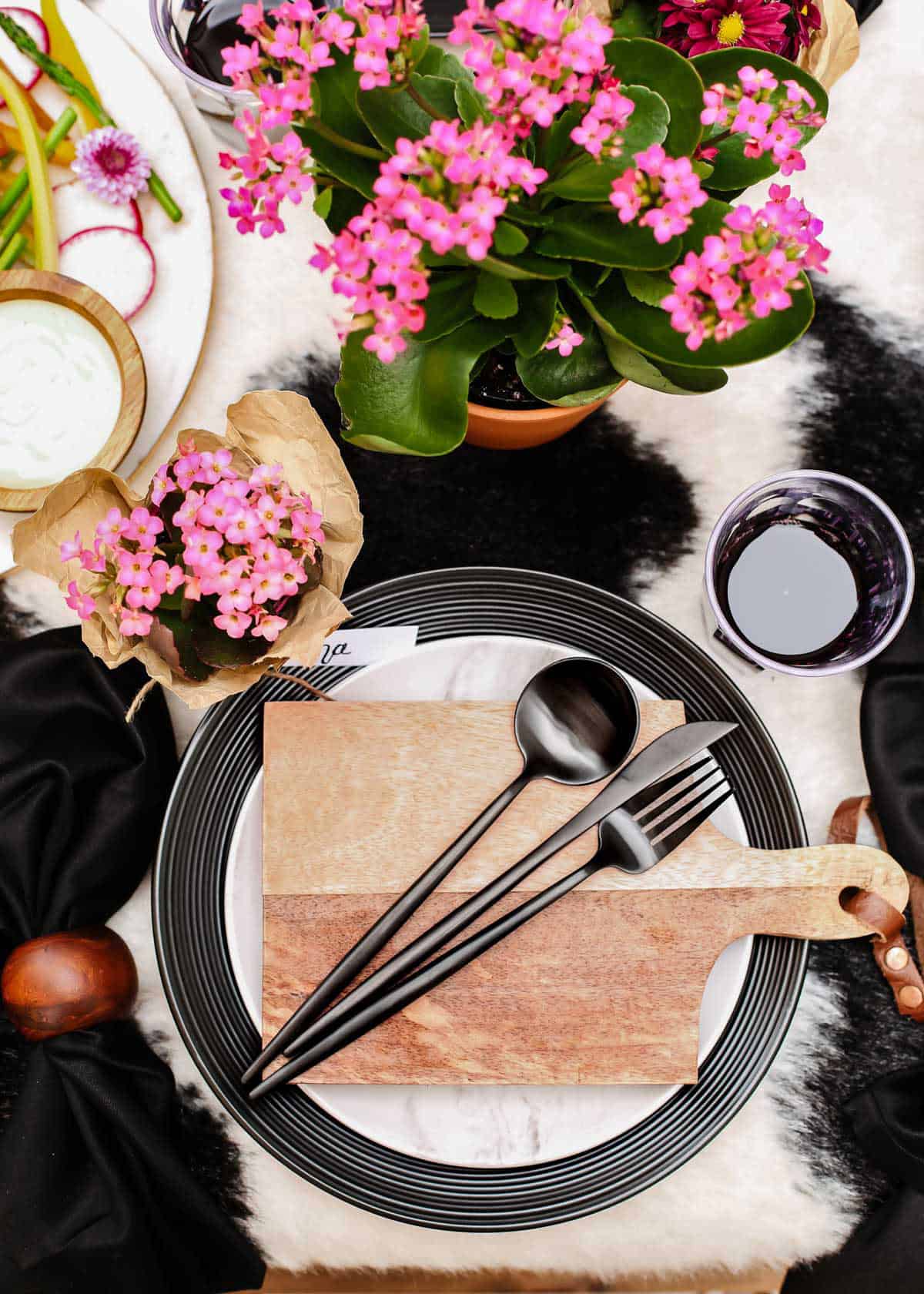 outdoor tablescape with layered black and white dishes and individual wood cutting board on top.
