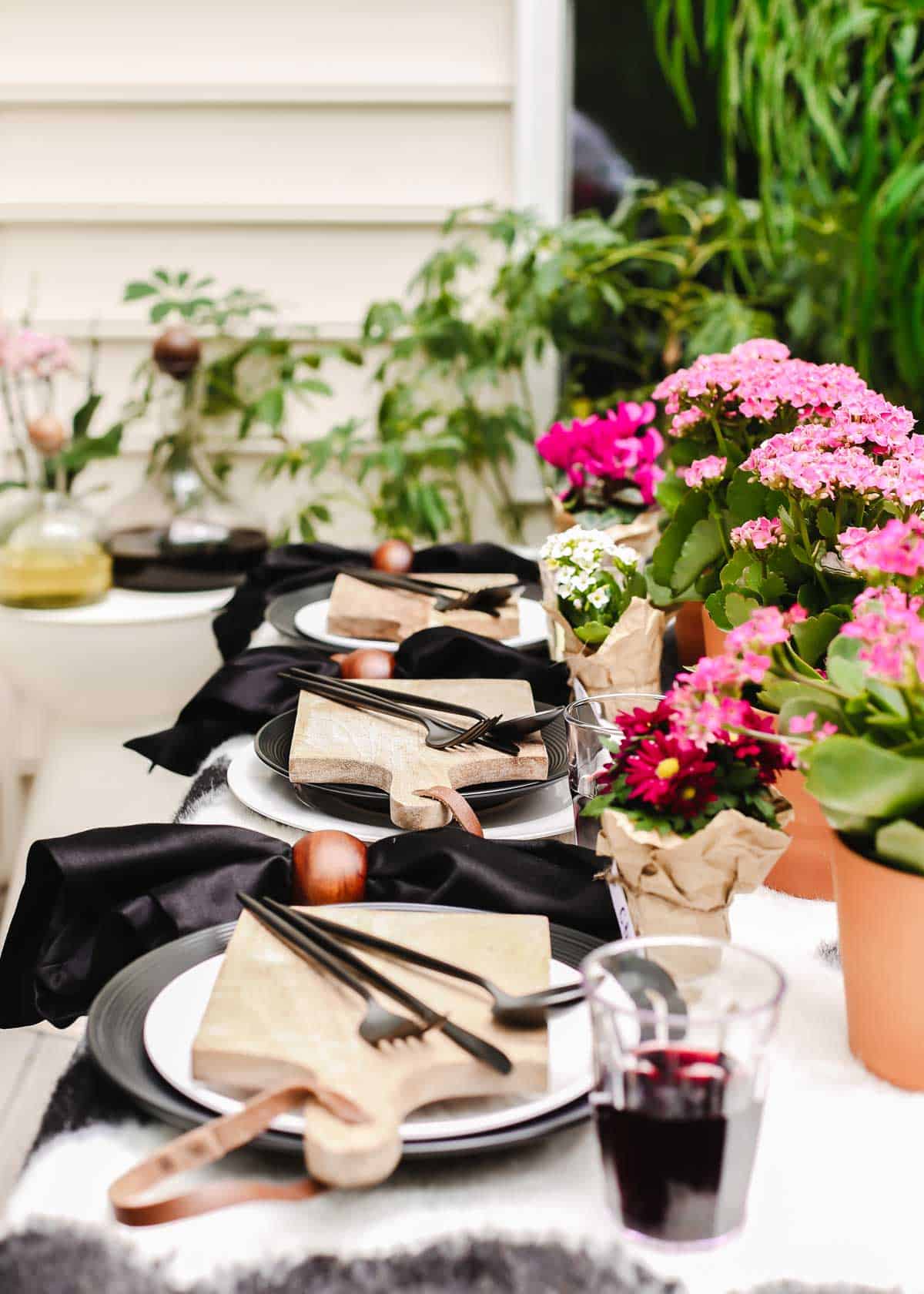 outdoor tablescape with black and white table cover, dishes, and pink potted flowers centerpiece.