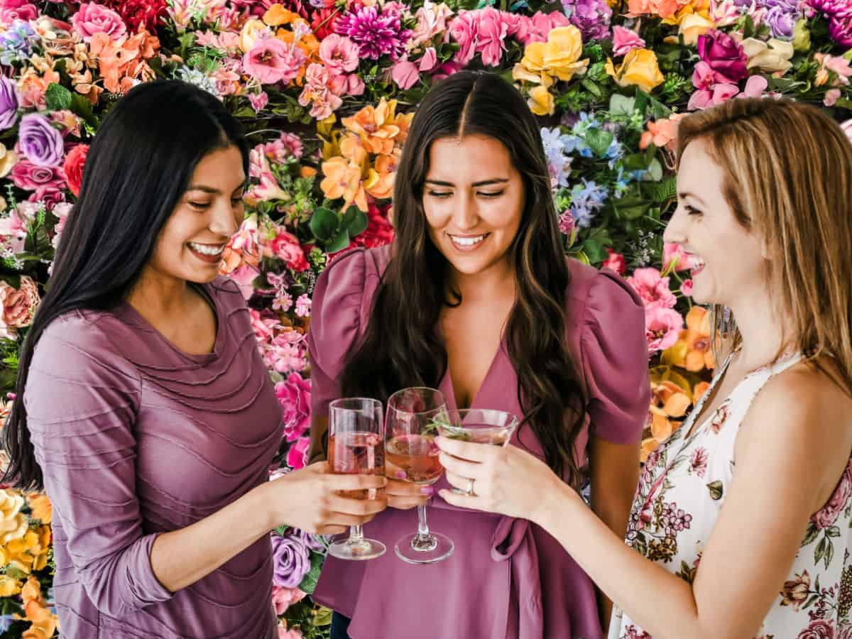 three ladies with champagne standing in front of a flower wall.