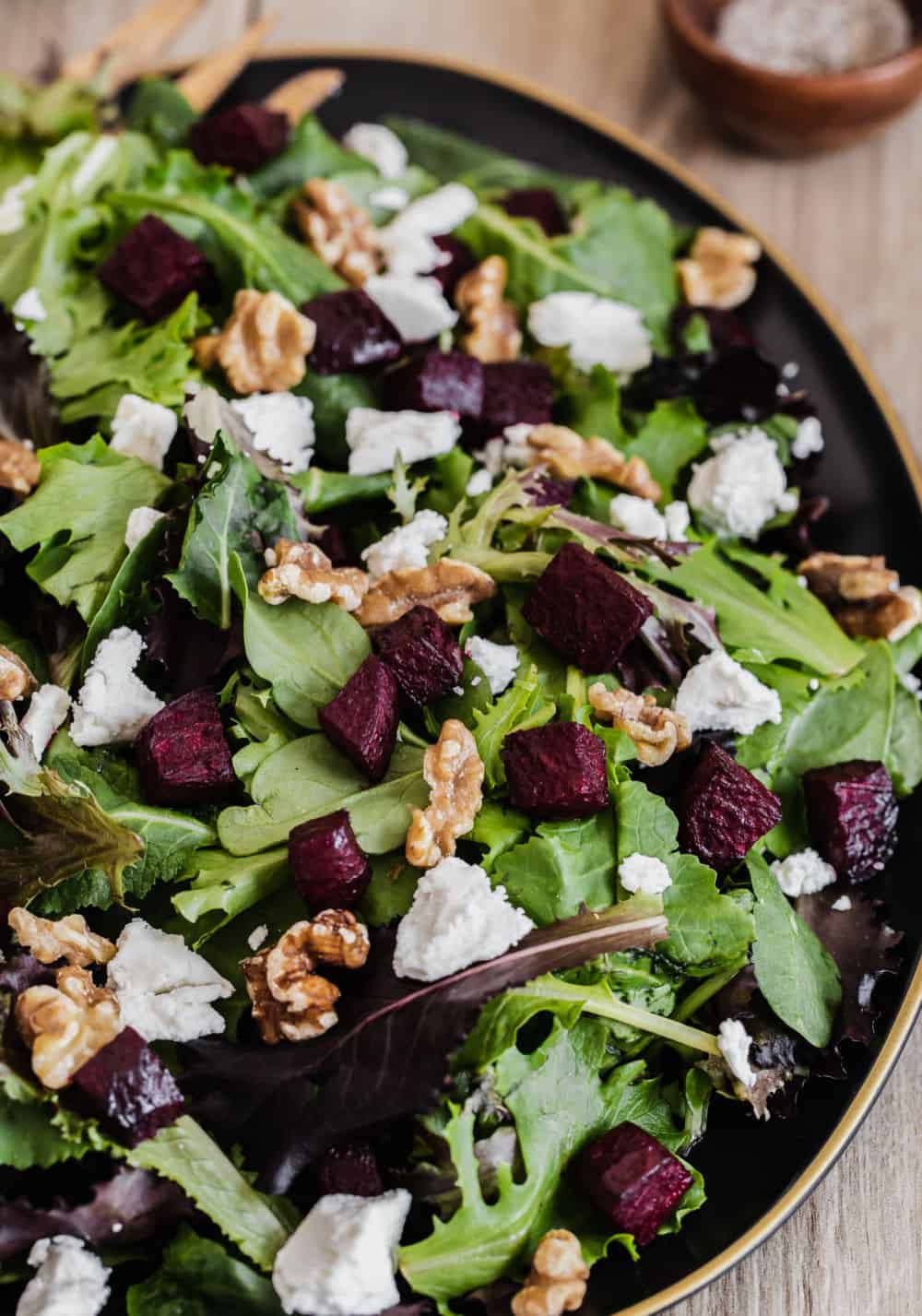 green salad with roasted beets and goat cheese and nuts on black platter.