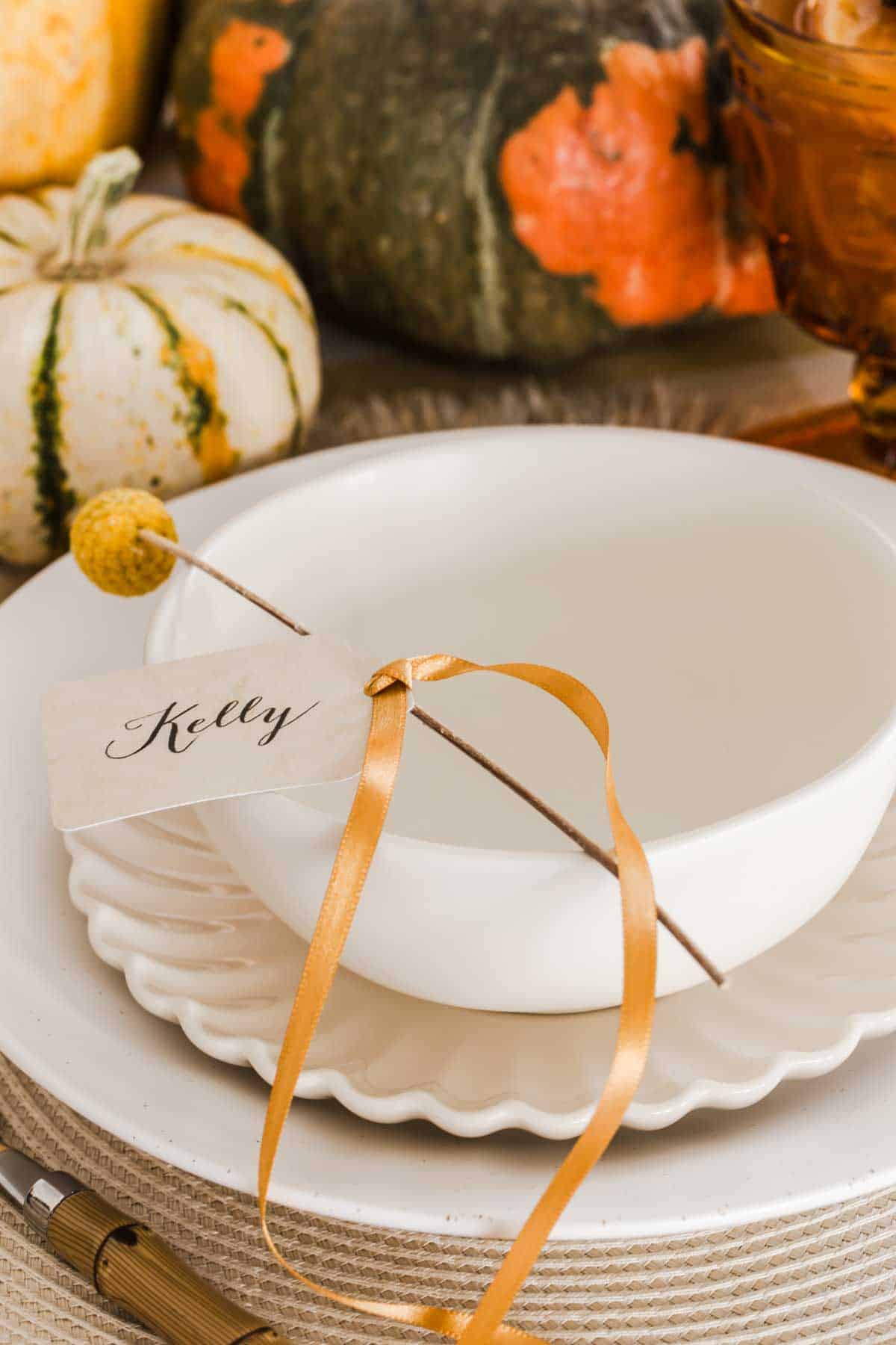 cream colored bowl on dinner plate, with yellow flower stem and place card tied on.