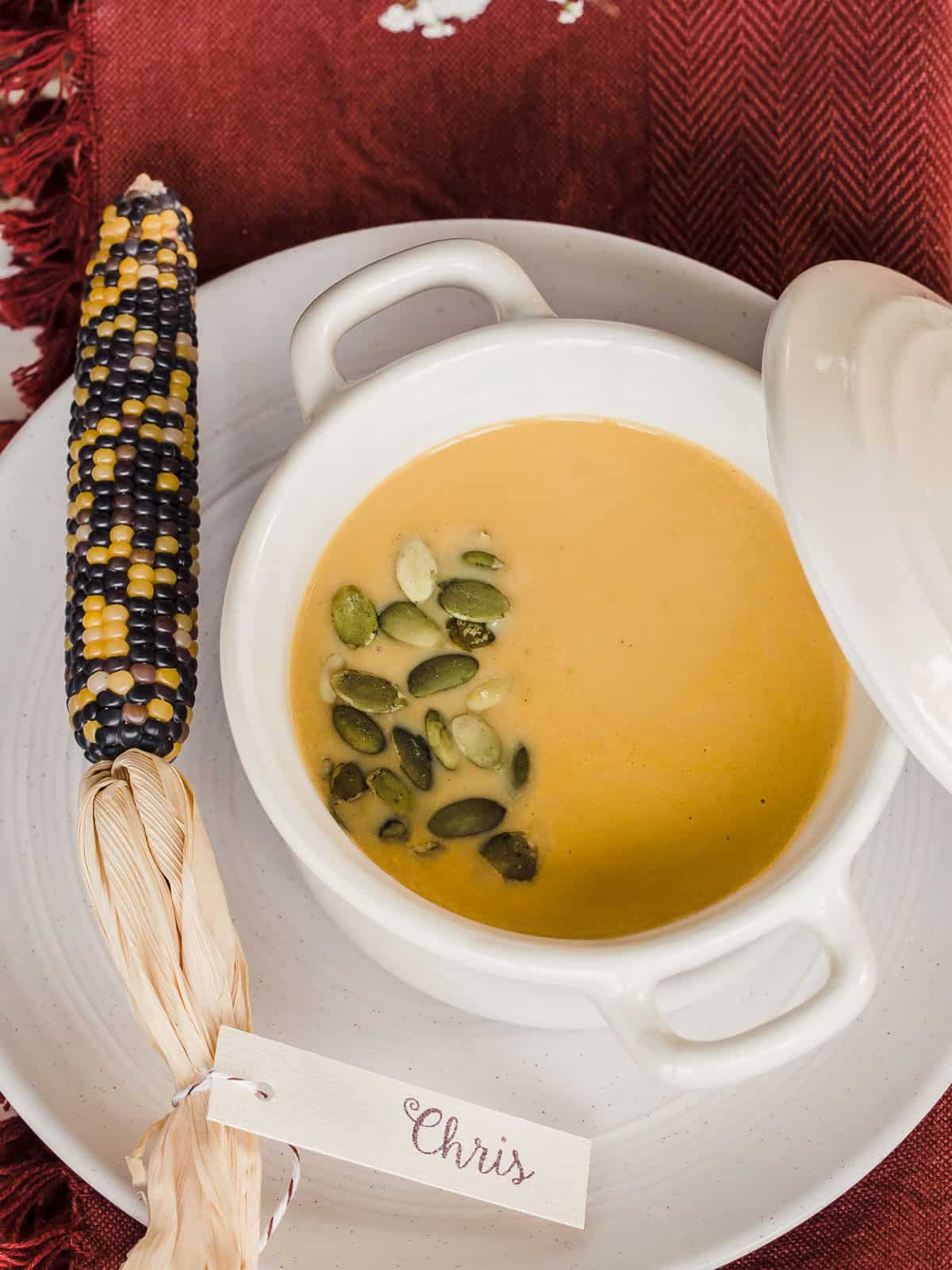 orange soup in white bowl on fall place setting, overhead.