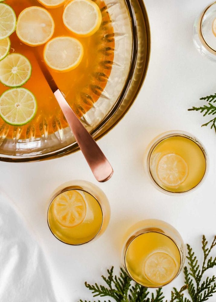 punch bowl garnished with lemons and limes, with 3 filled glasses.