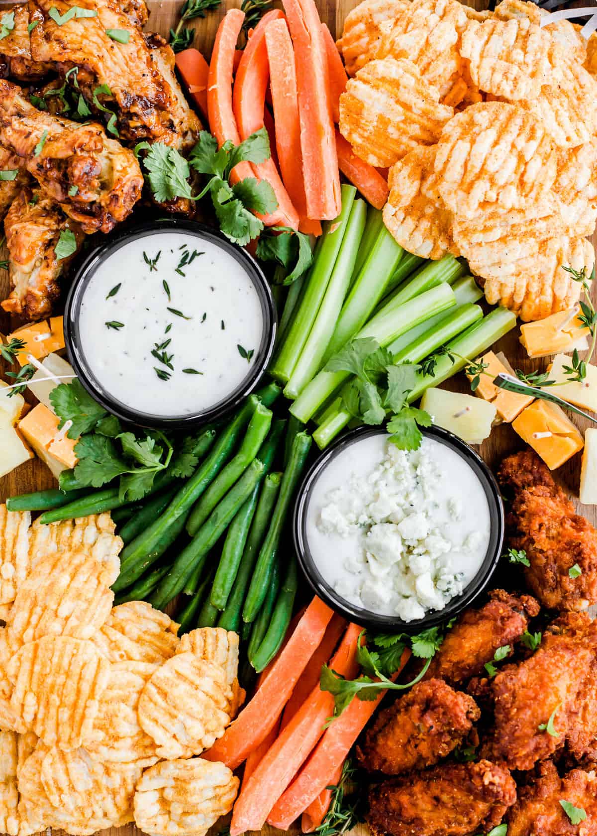 overhead closeup of two white dips surrounded by vegetable sticks and chips.