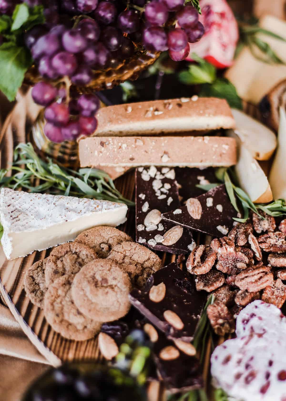 brie, biscotti, chocolates, cookies, and nuts on wood board.