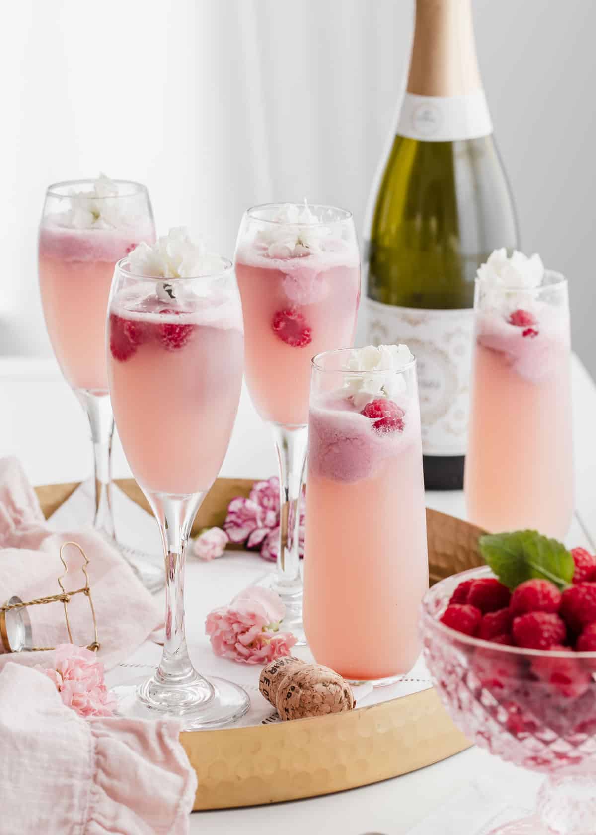 flute glasses filled with raspberry sherbet mimosas on gold tray with champagne bottle in background.