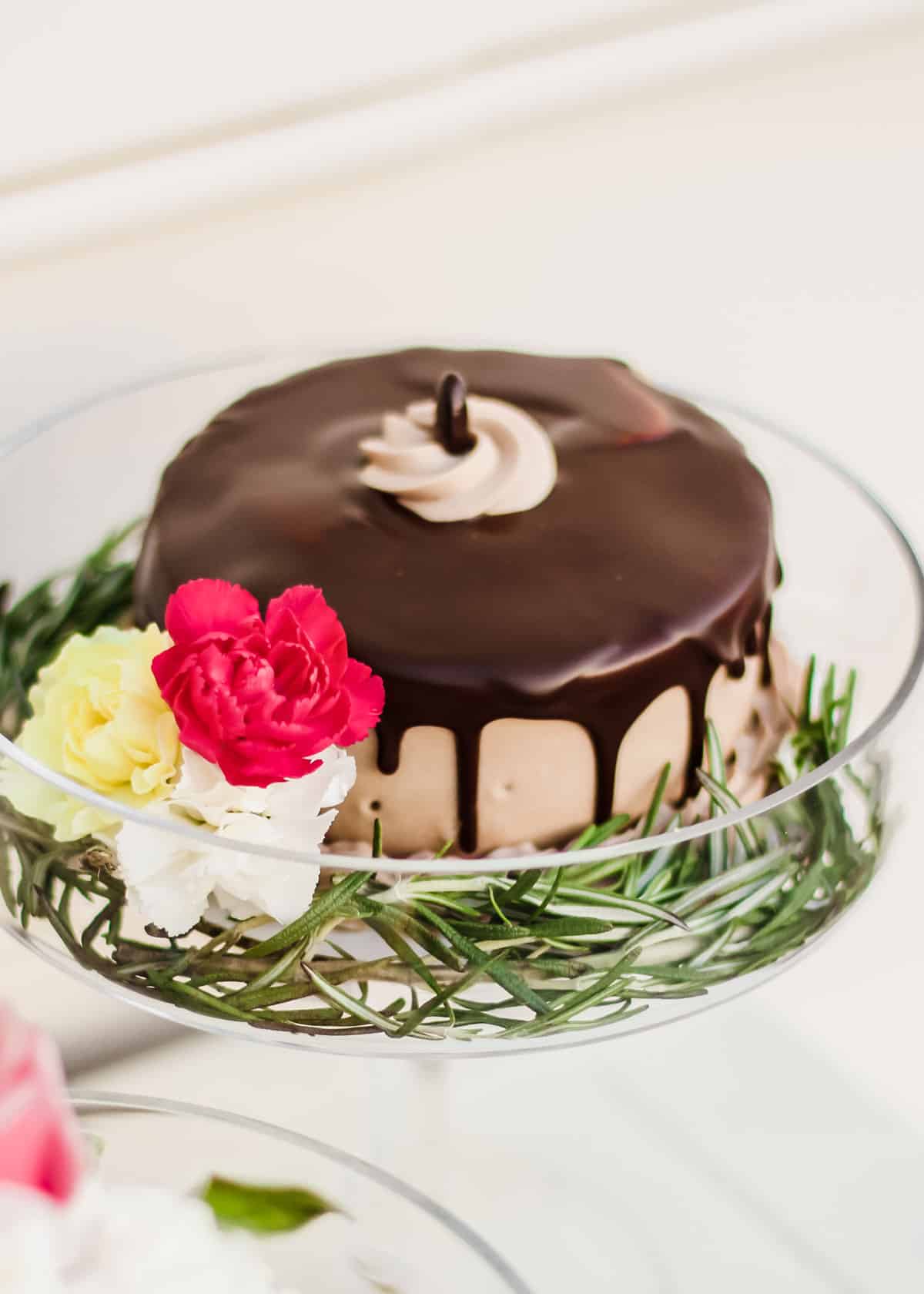 chocolate mini cake on glass pedestal with fresh flowers on the side.