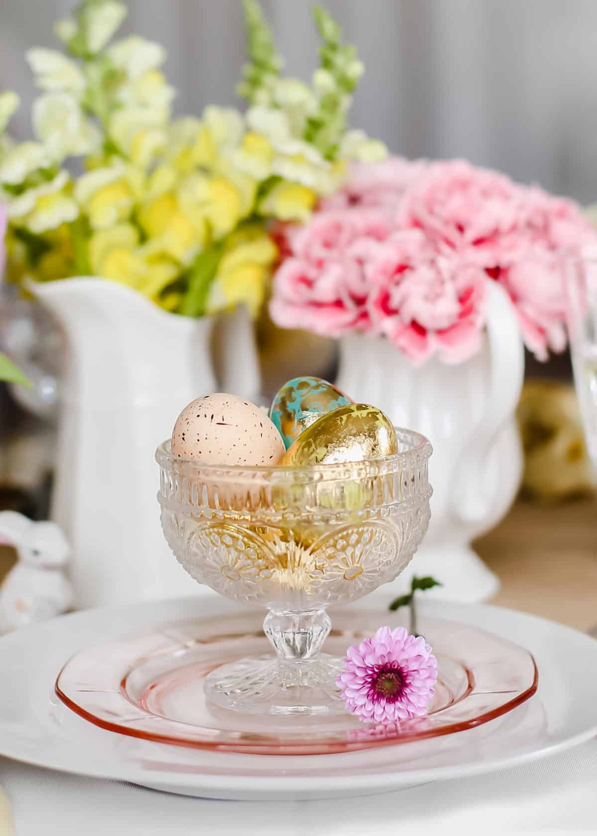glass compote dish holding decorative eggs for Easter place setting.