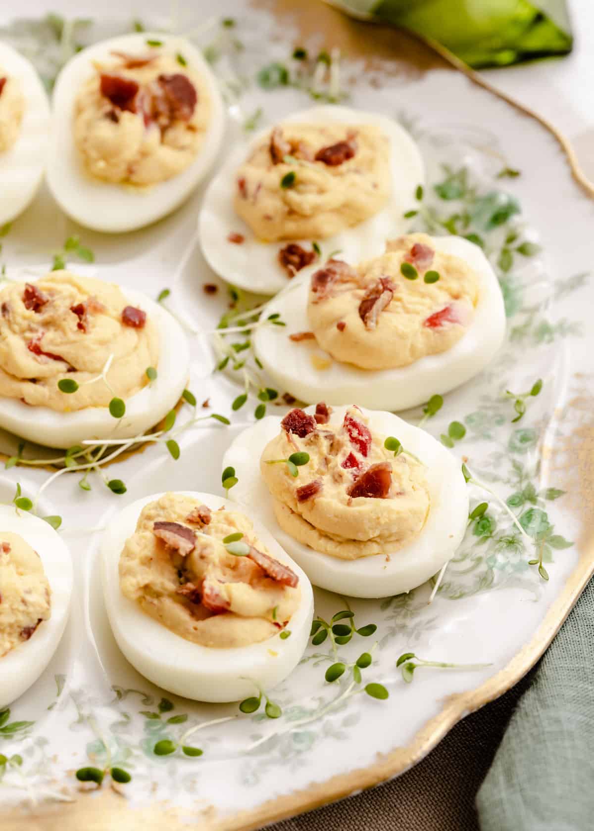 deviled eggs topped with bacon sitting on vintage plate, close up view.