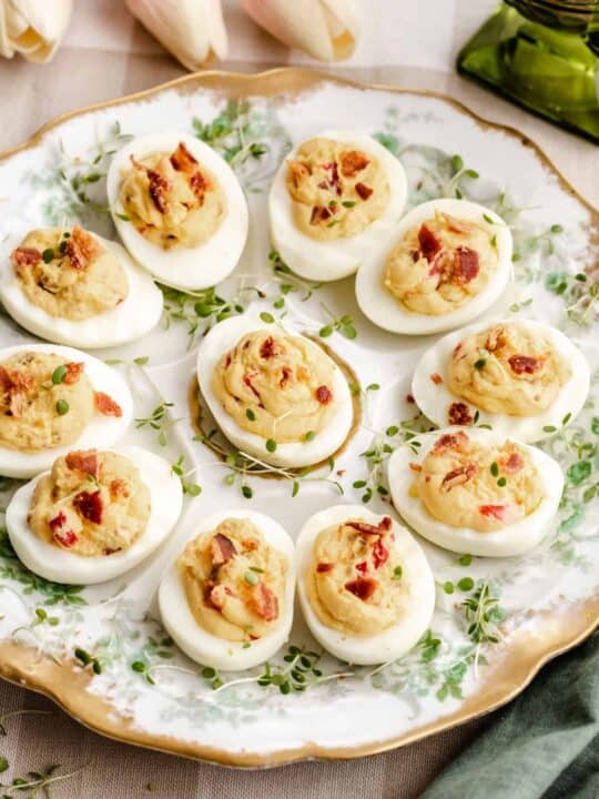 round vintage oyster plate filled with deviled eggs topped with bacon.