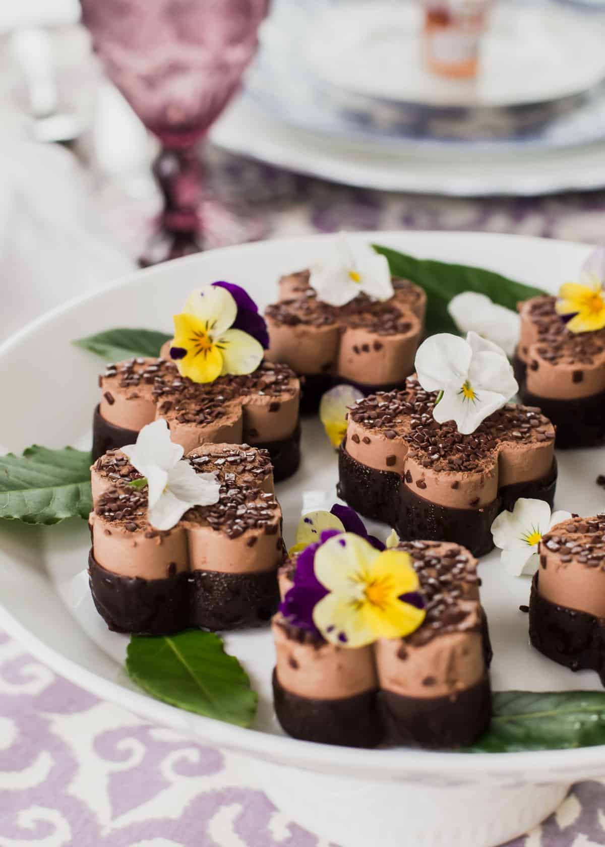 mini chocolate desserts with tiny edible flowers on top, on white platter.