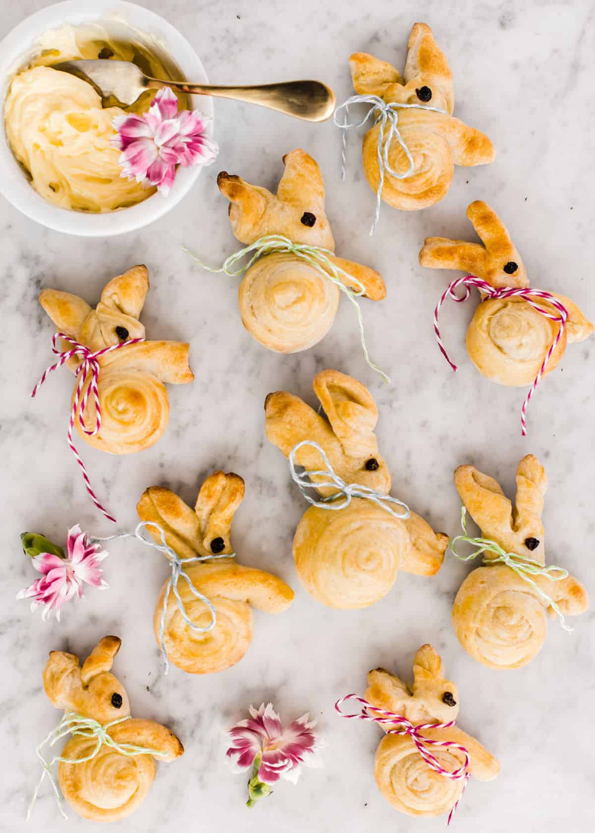 bunny shaped bread rolls on white marble with small bowl of butter on the side.