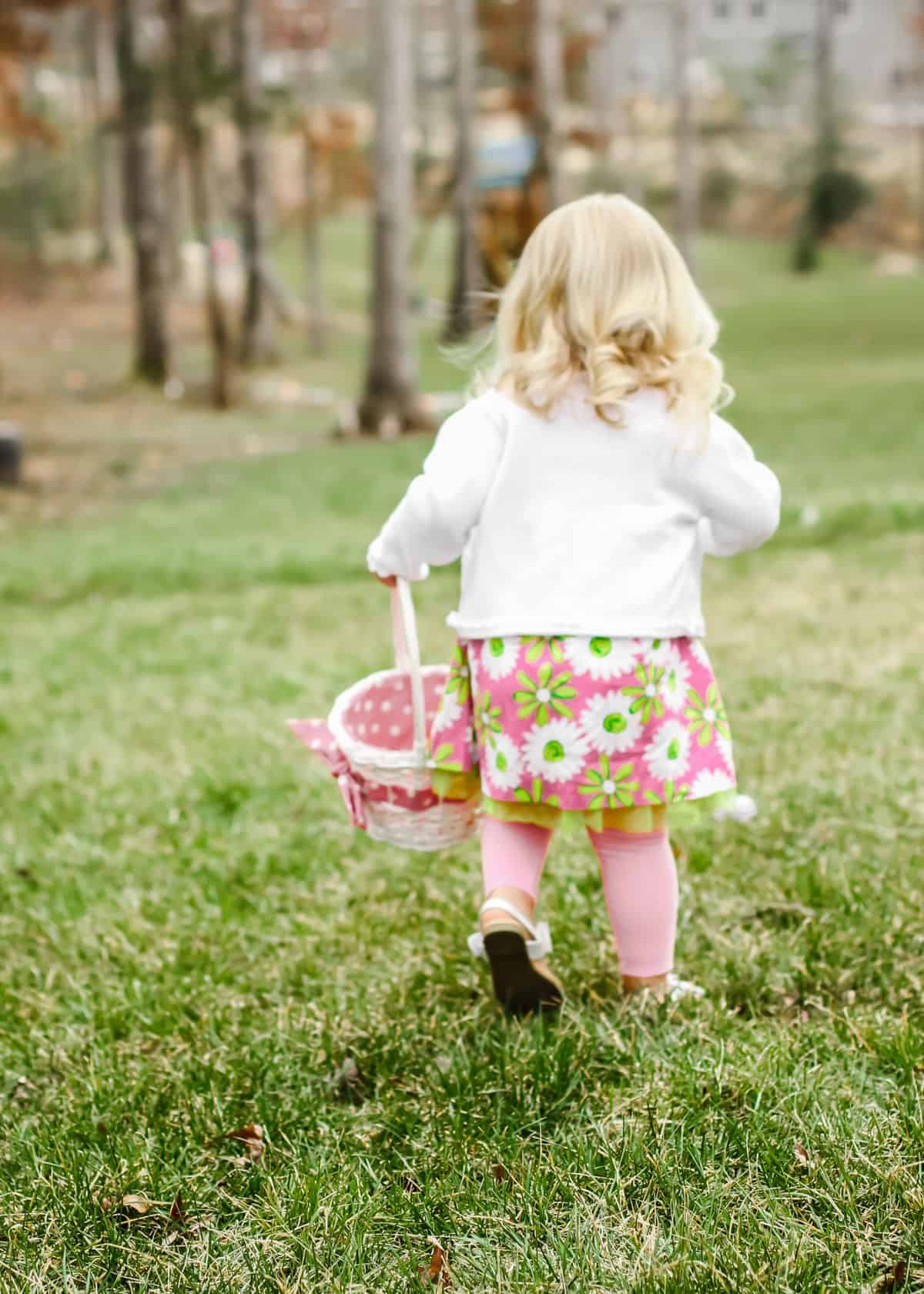 little girl in backyard doing an Easter egg hunt with basket.