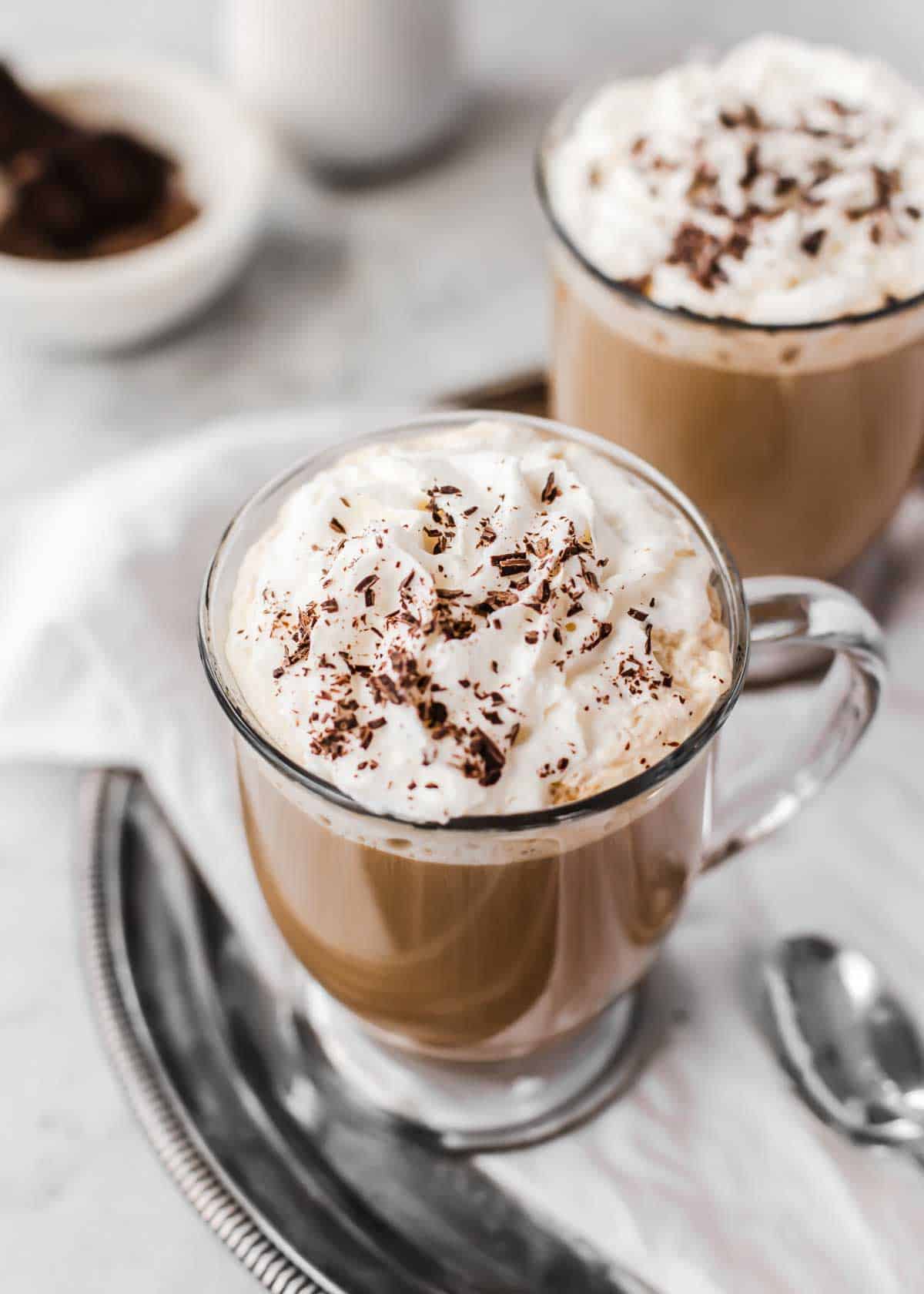 coffee drink in glass mug, topped with whipped cream and chocolate shavings.