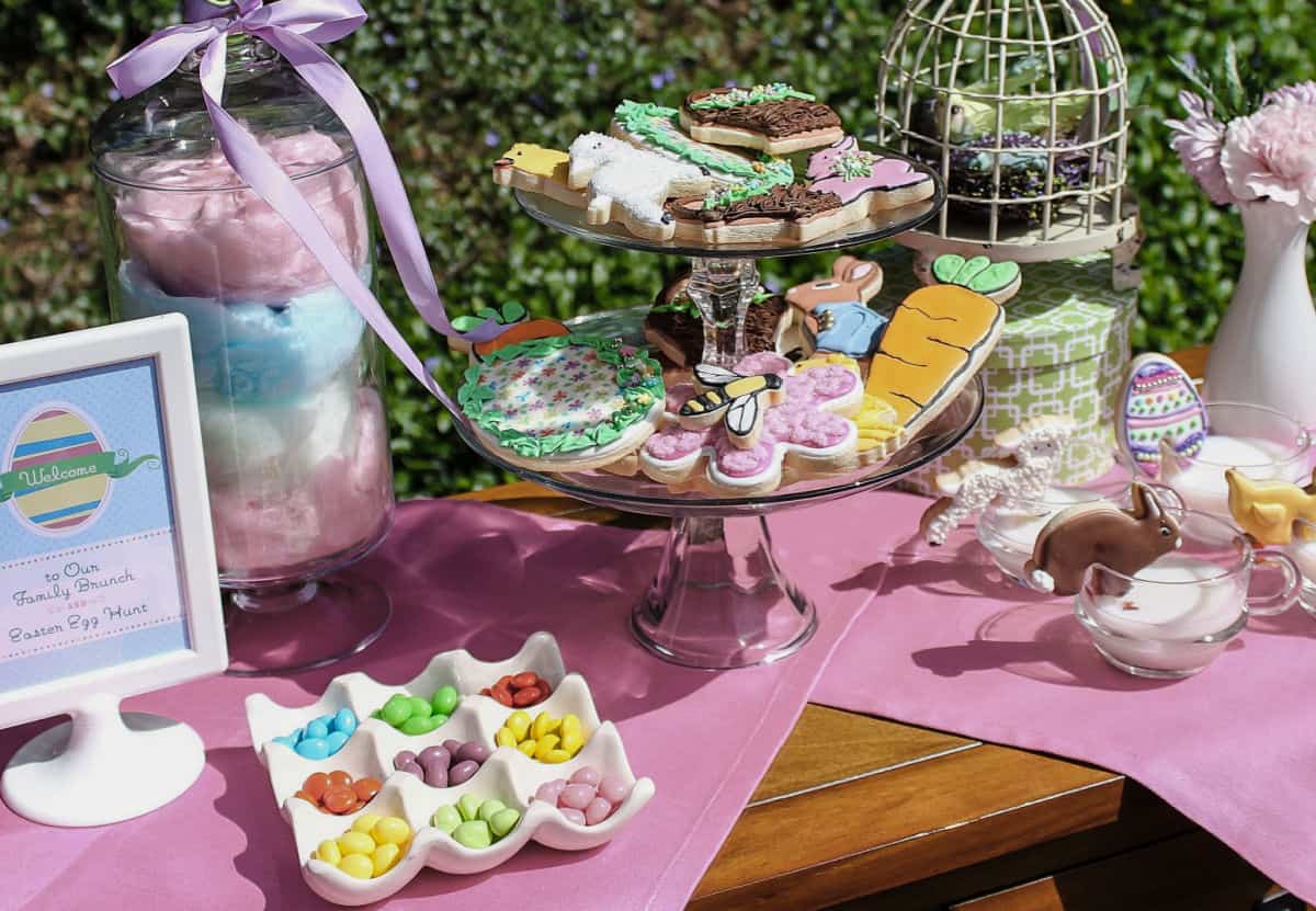 Easter dessert table for kids with jelly beans, cotton candy, and decorated cookies, set up outside.