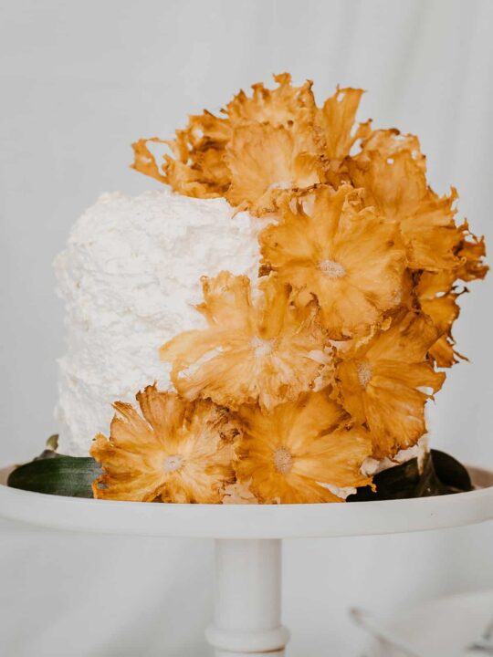 white layer cake decorated with dried pineapple flowers cascading down the side.