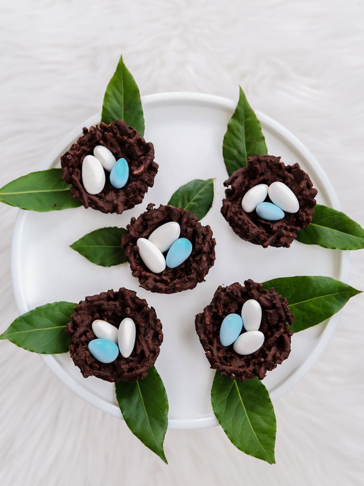 chocolate nests with blue and white candy eggs, on white platter.