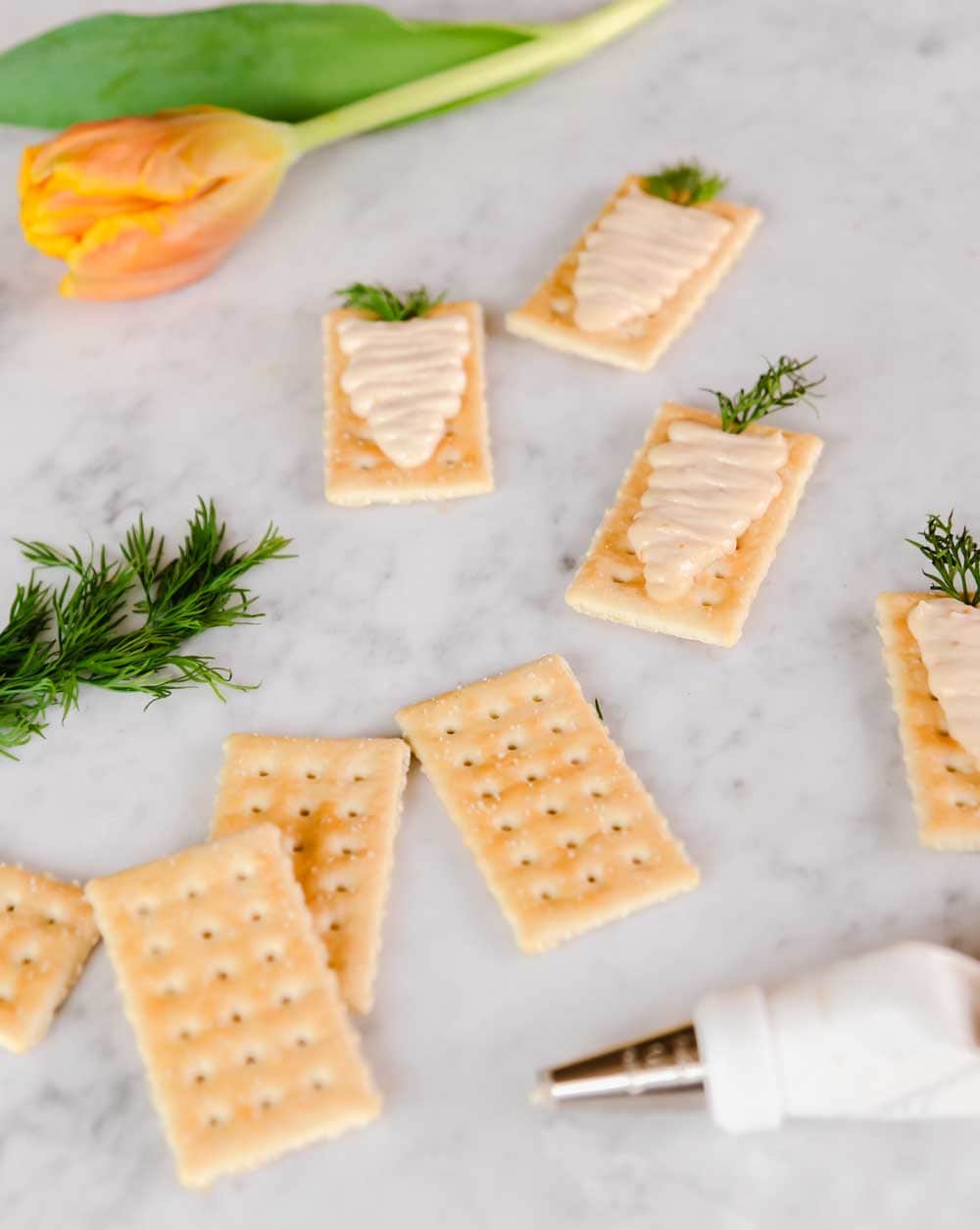 ingredients and piping bag to make Easter cracker appetizers, on marble surface.