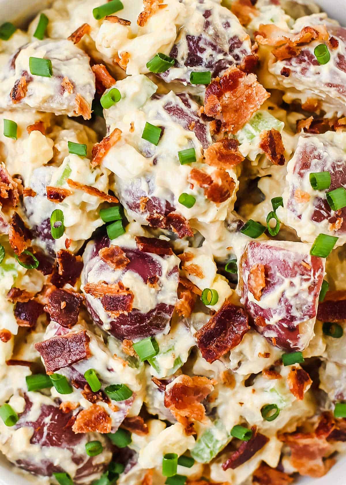 close up view of small red potato salad with bacon and chives on top.