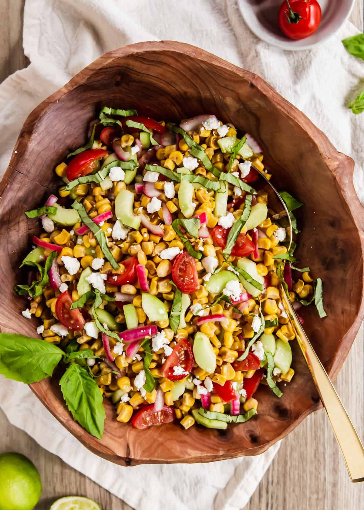 corn salad with tomatoes, cucumbers and fresh basil in wood serving bowl.