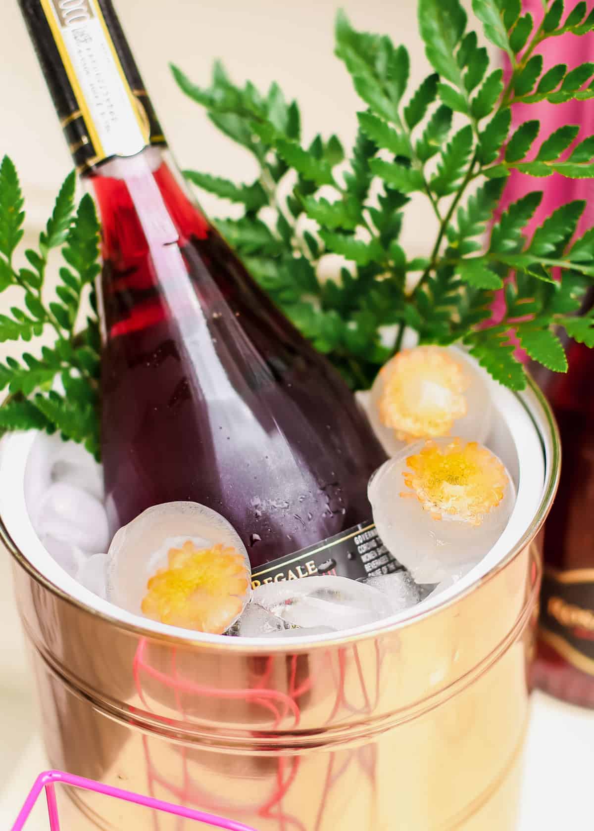 rose champagne in ice bucket with floral ice spheres and green ferns.