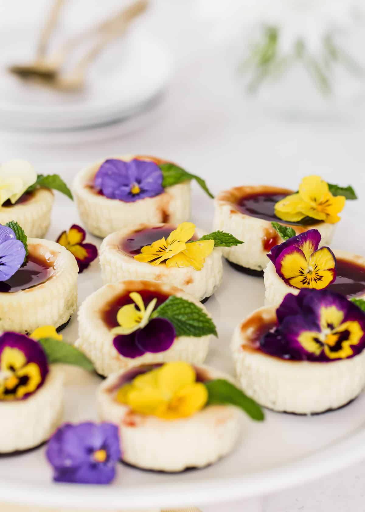 mini cheesecakes on white platter garnished with yellow and purple flowers.