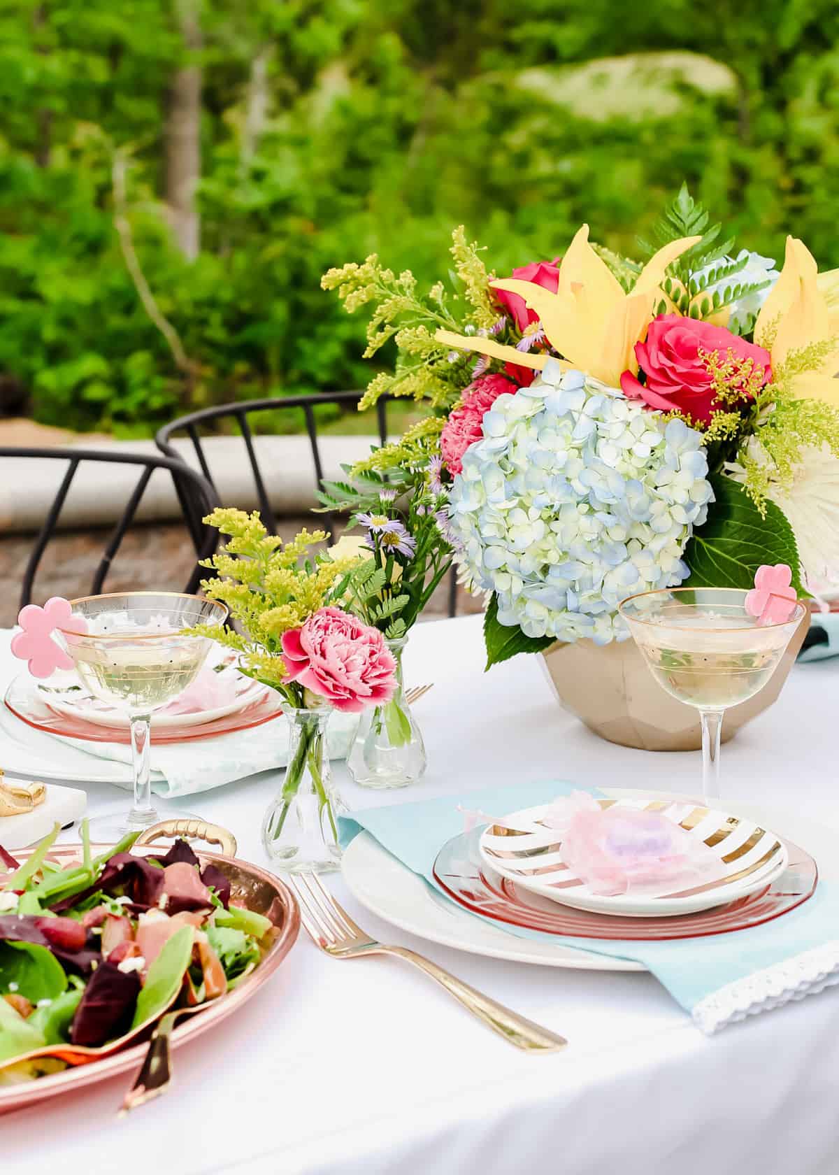luncheon table setting outdoors with flowers centerpiece and layered plates with coupe glasses.