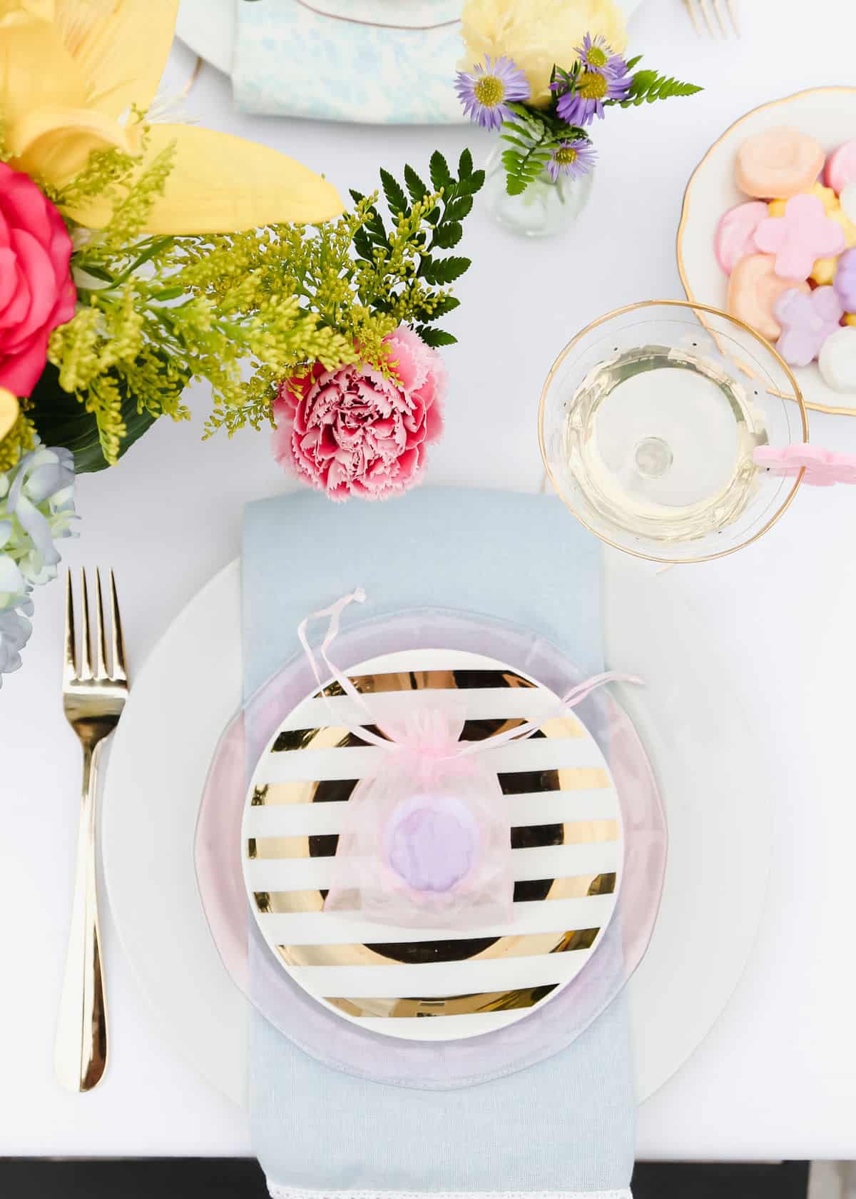 place setting overhead with white plate layered with pink glass plate and gold and white stripe plate with blue napkin.