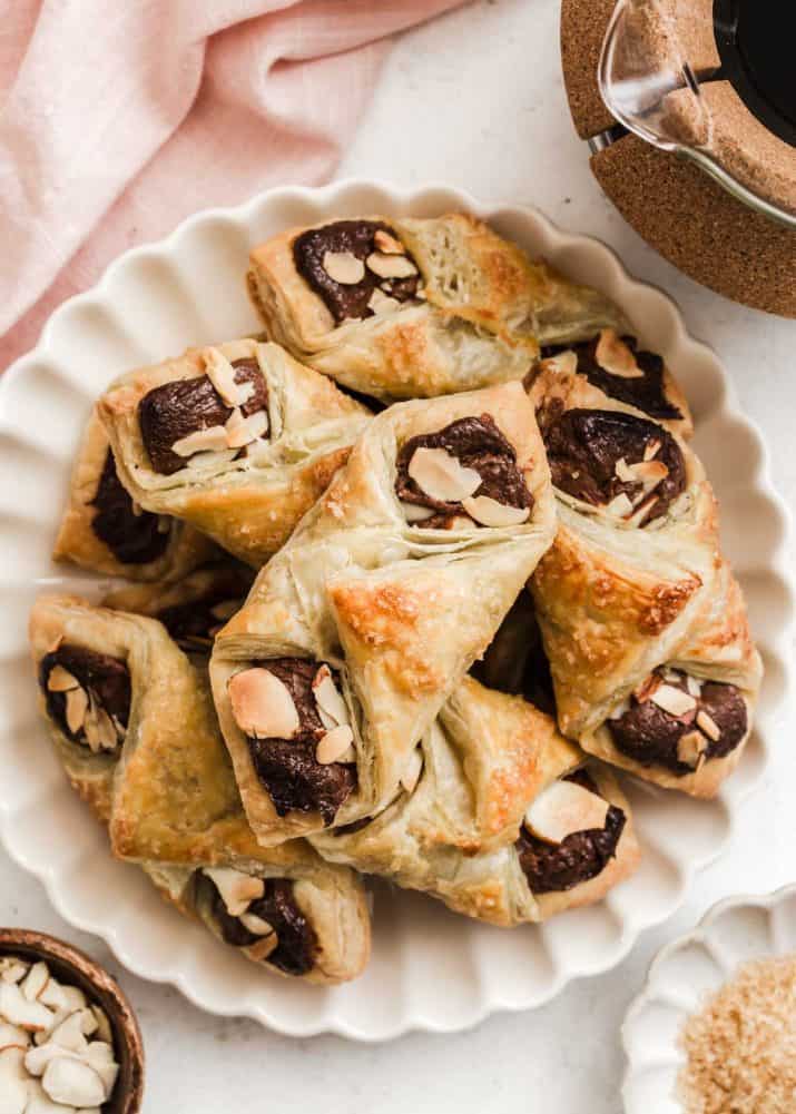 puff pastry packets with chocolate and almonds piled on a scalloped plate.