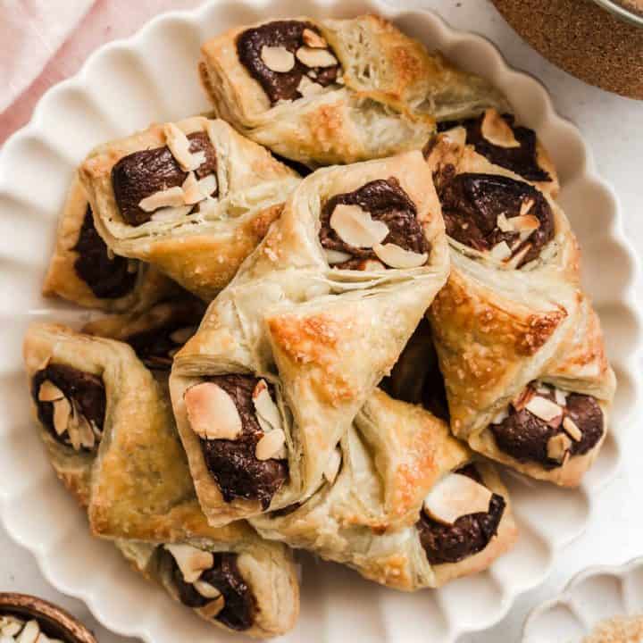 puff pastry packets with chocolate and almonds piled on a scalloped plate.