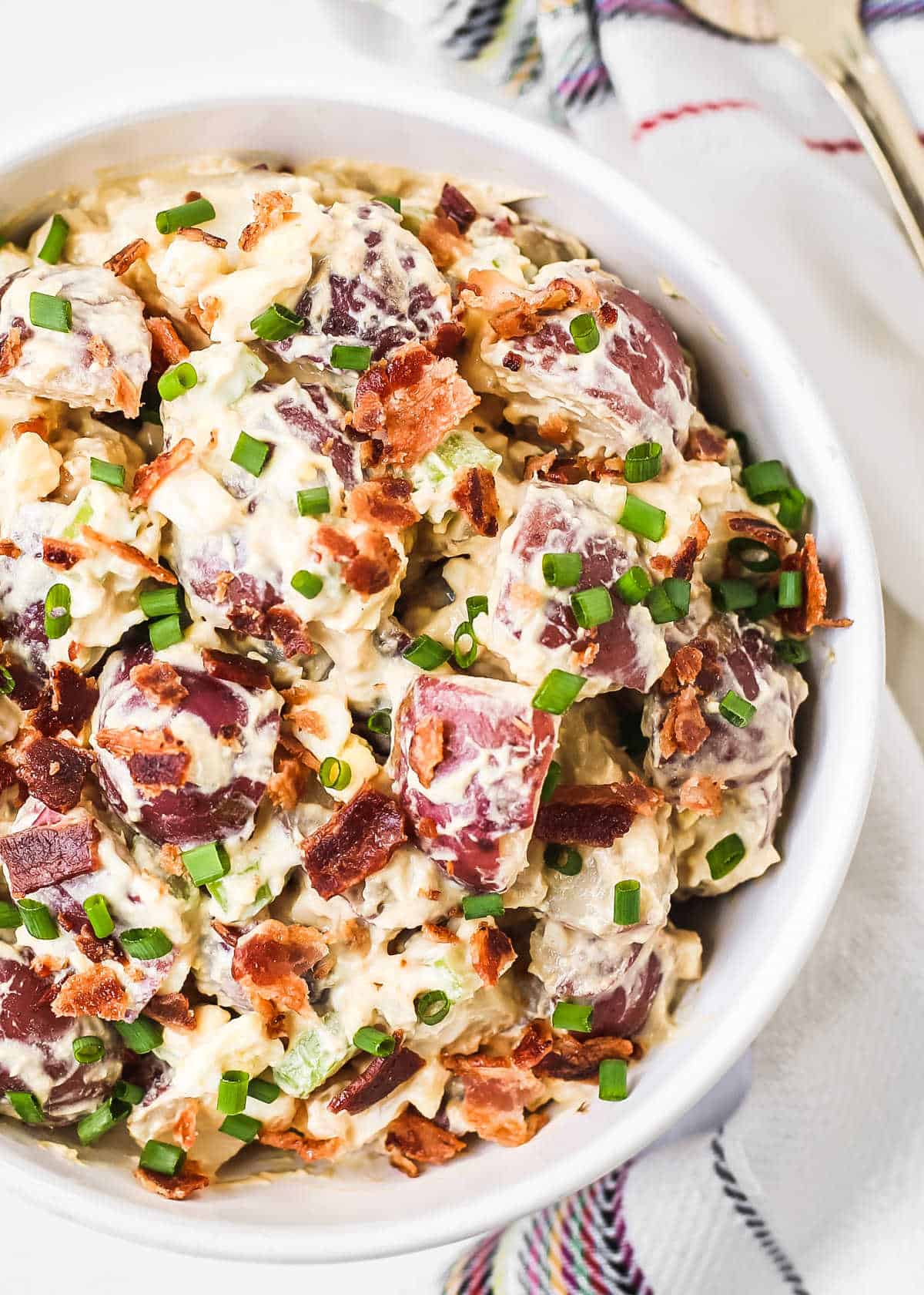 potato salad with red potatoes in creamy dressing with bacon and chives, overhead.