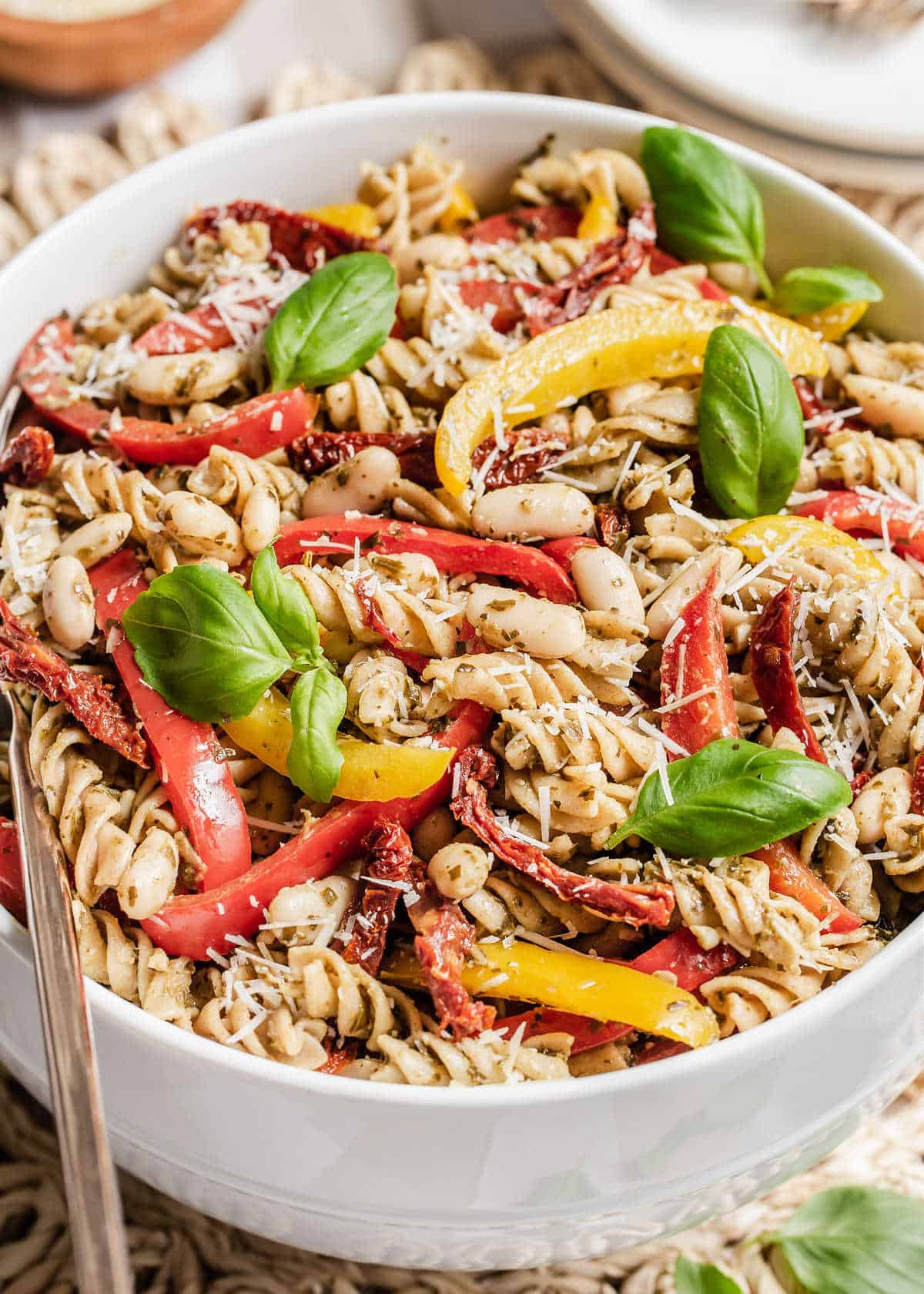 large white bowl of pesto pasta salad with basil on top.