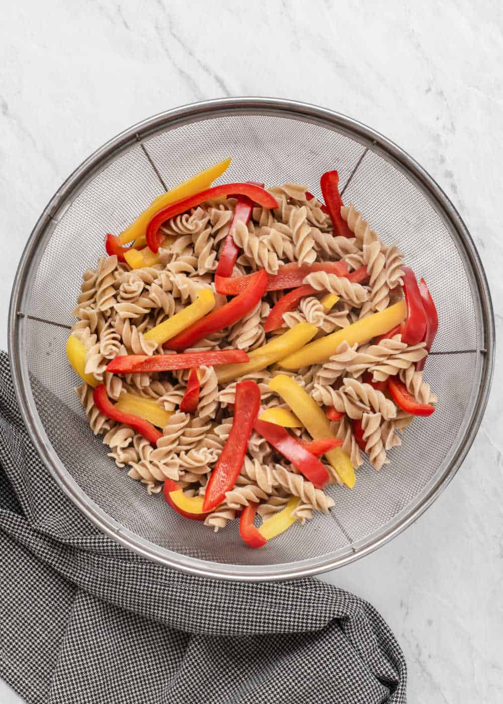 cooked rotini pasta and red and yellow pepper strips in large strainer.