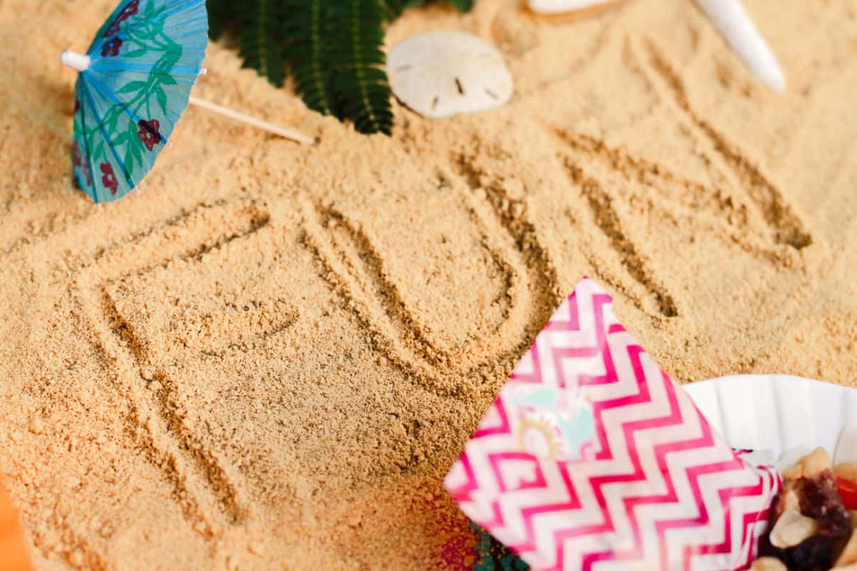 sand with the word FUN written in it, and shells and drink umbrellas around.