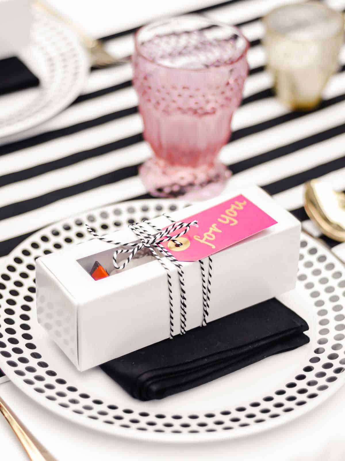 dinner place setting with black and white dishes and white box party favor on top of plate.