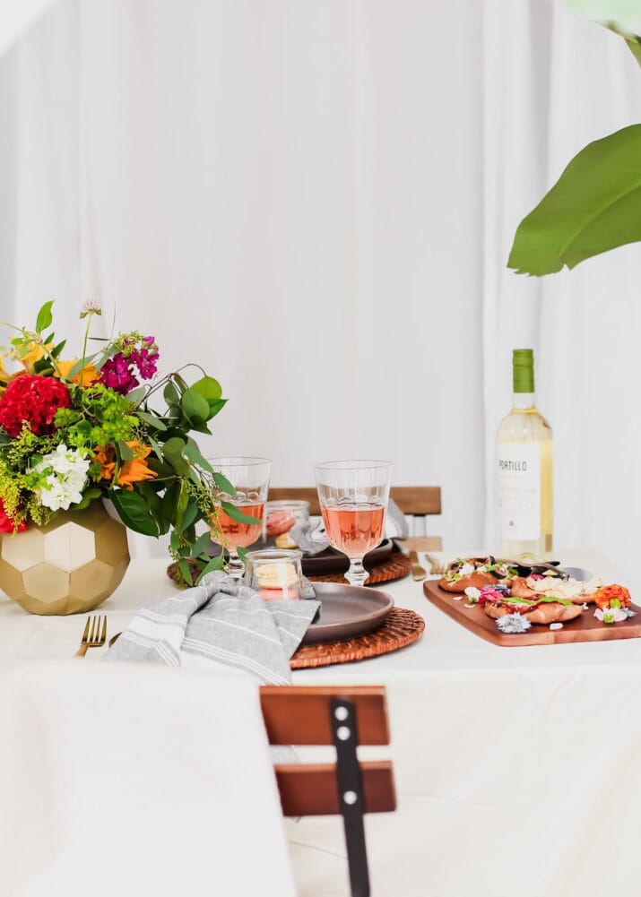 outdoor dinner table with flowers and wine and food platters.