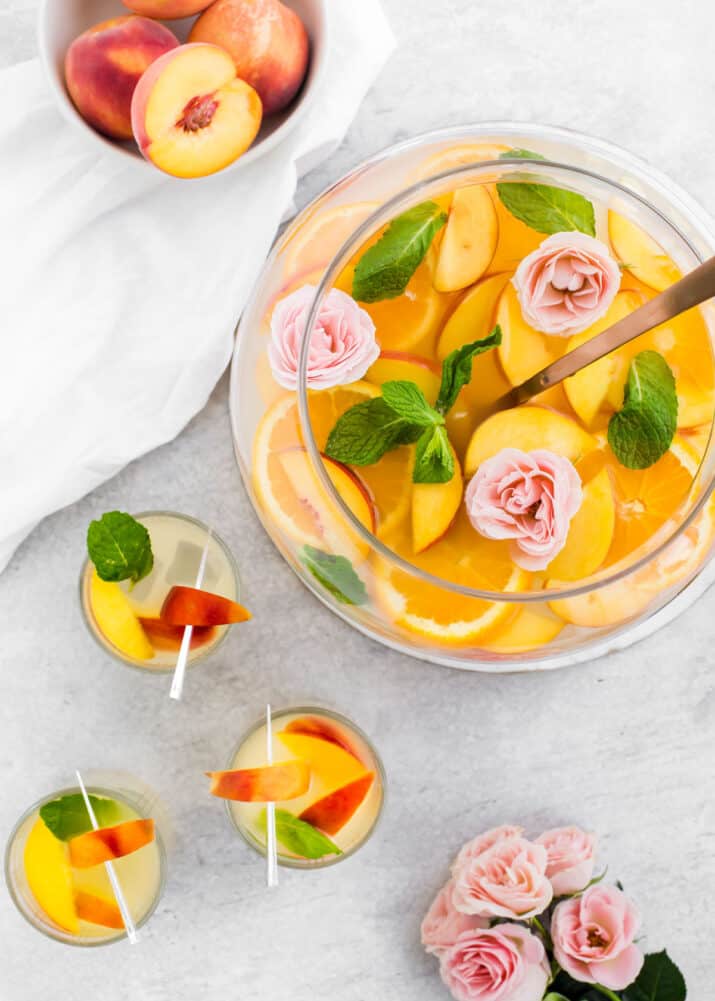 punch bowl filled with orange and peach punch surrounded by filled glasses, on light gray table.