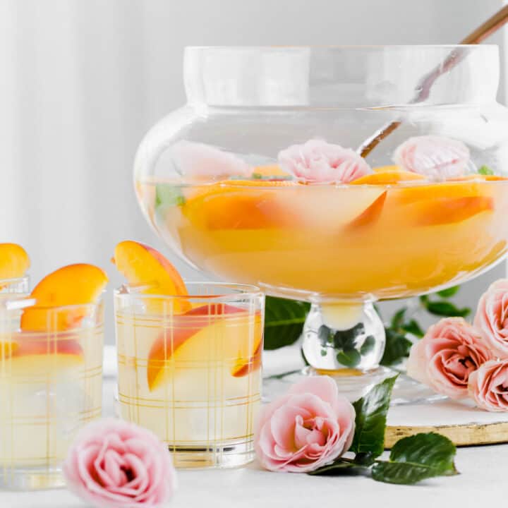 glass footed bowl with orange tinted punch inside and filled glasses on table.