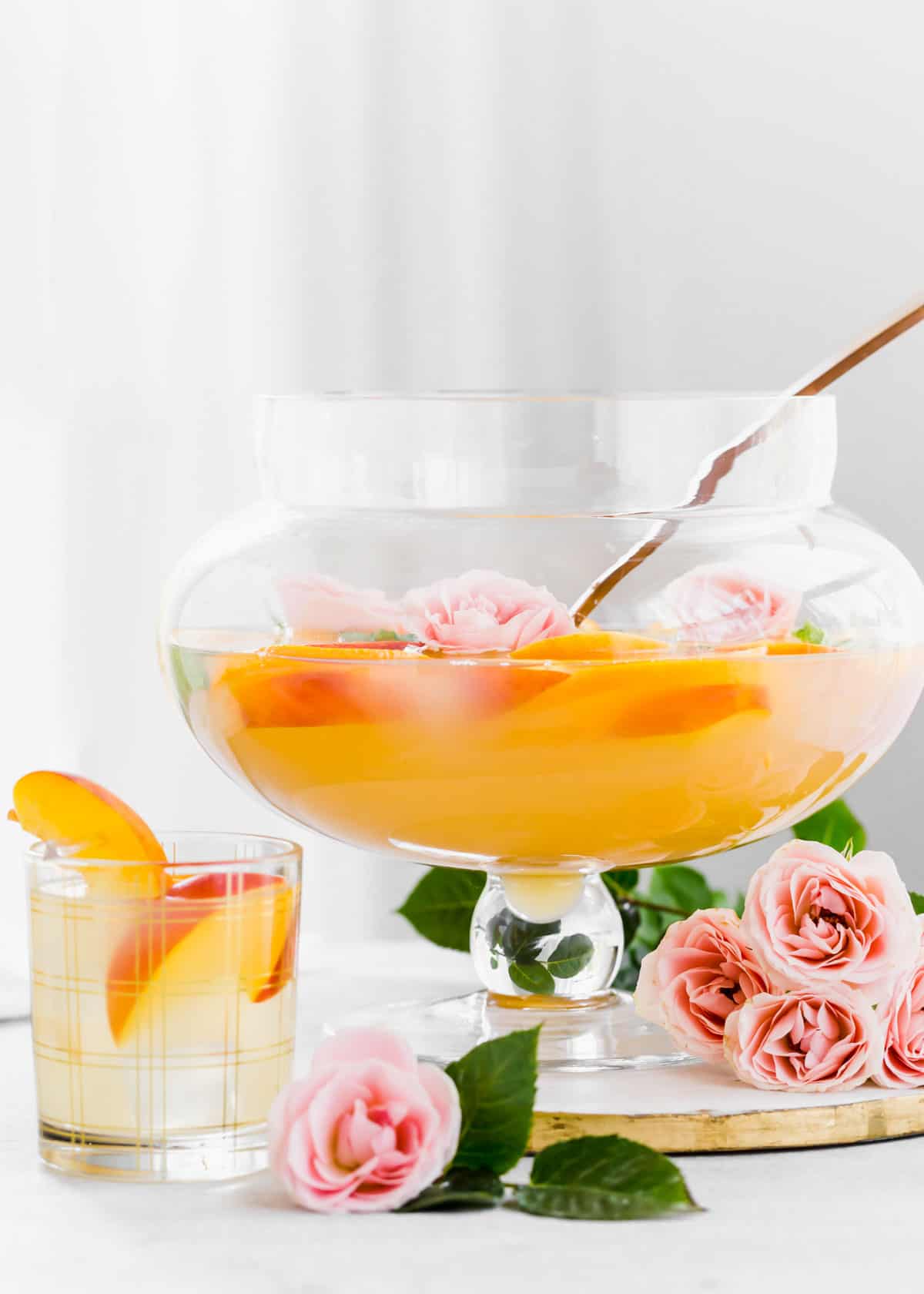 peach colored punch in glass footed bowl with ladle, and filled glass on table.
