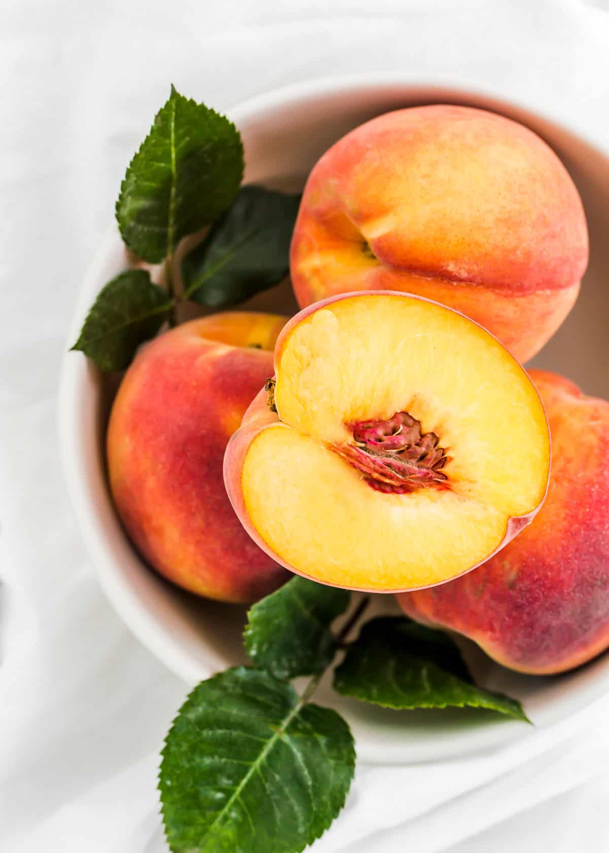 bowl of peaches with one peach sliced in half, overhead view.