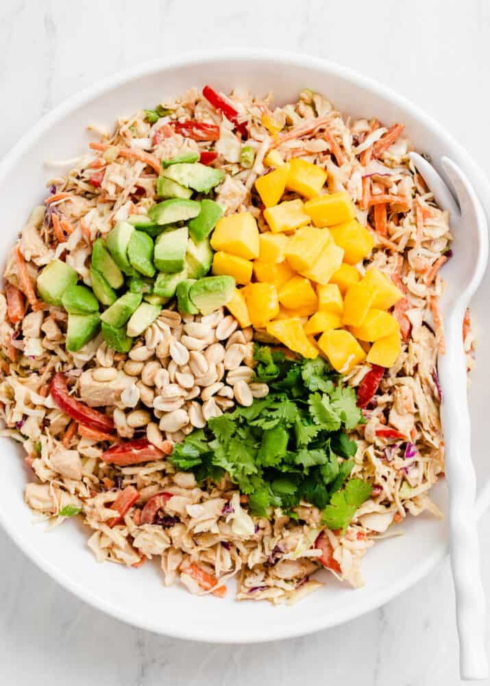 Mixed chicken cabbage salad with toppings in white bowl.