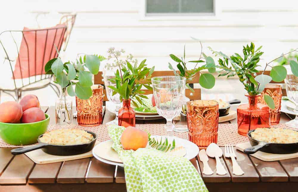 outdoor tablescape with orange glass vases with greenery inserted for centerpiece.