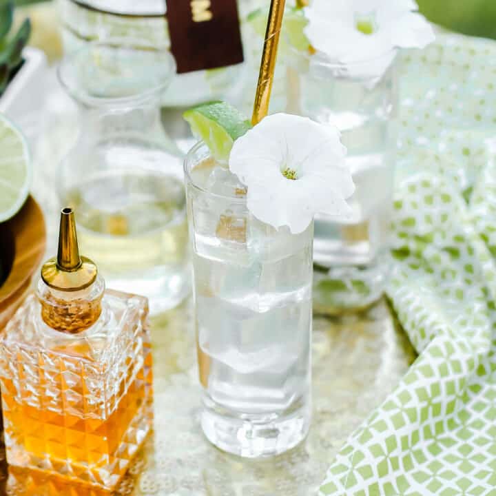 two glasses of mojitos garnished with white flowers, on gold tray.