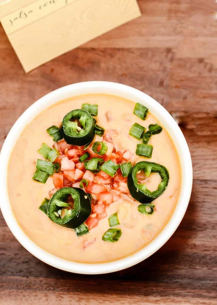 queso dip in small bowl, garnished with chopped tomatoes, onions, and jalapenos.