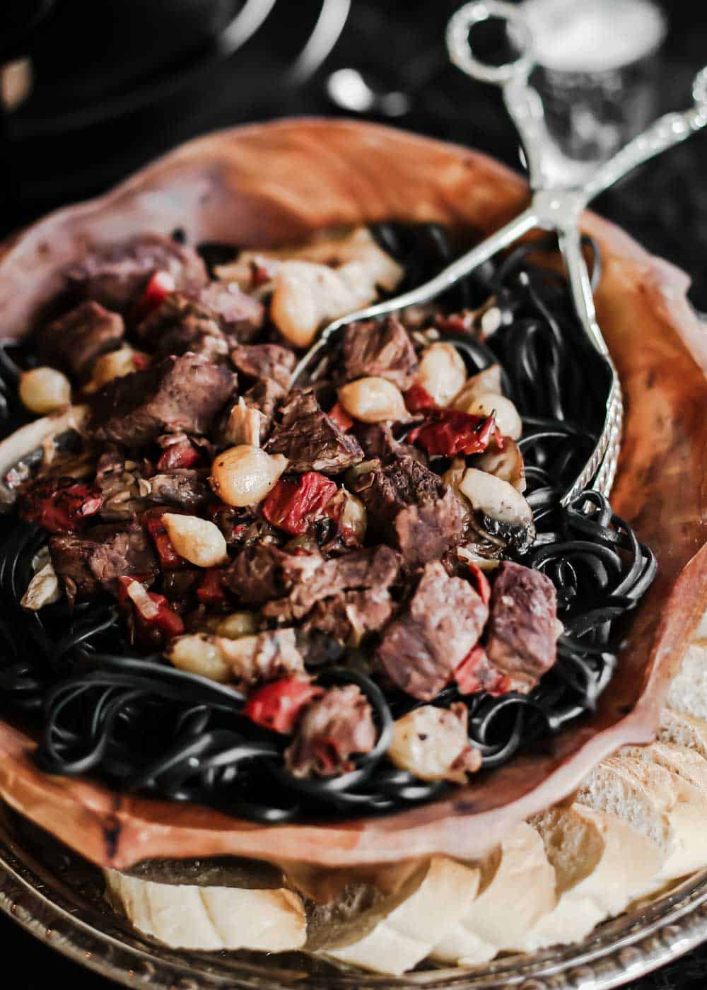beef tips with mushrooms and onions served over black noodles in wood serving bowl.