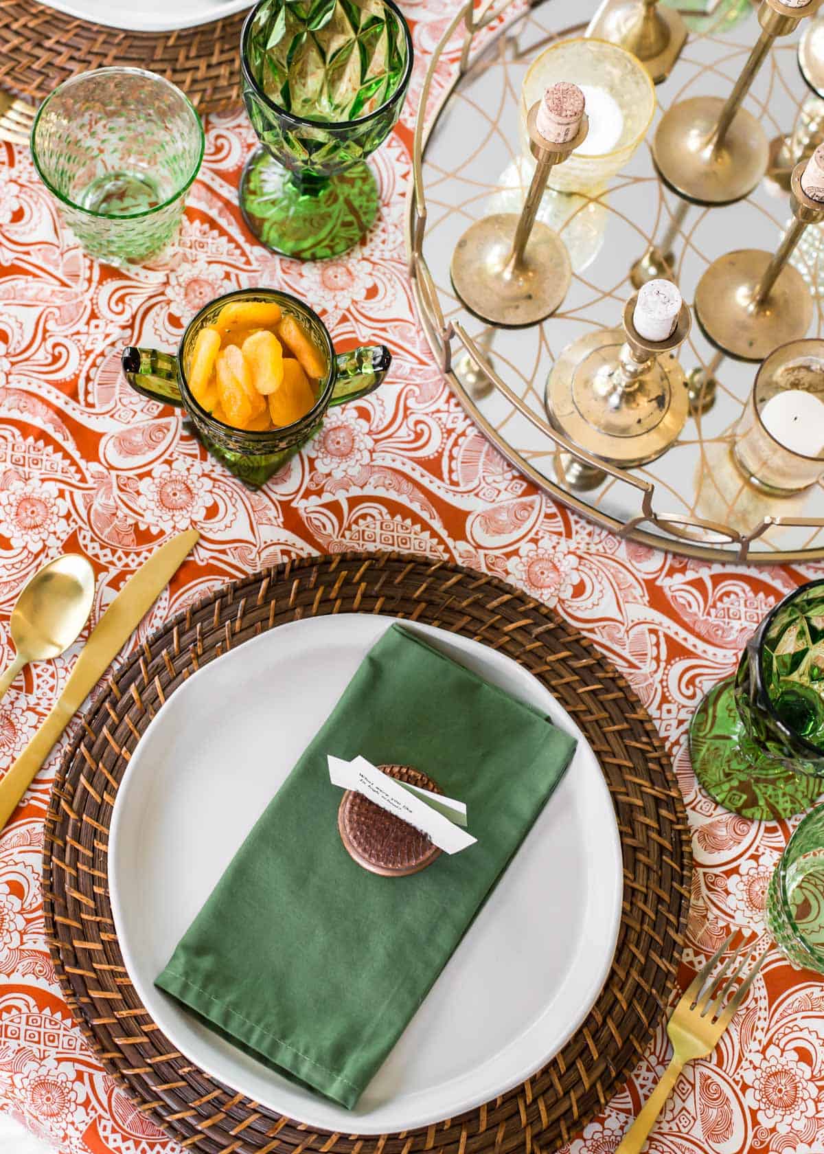 table setting with orange print table cloth and green napkins and glassware.