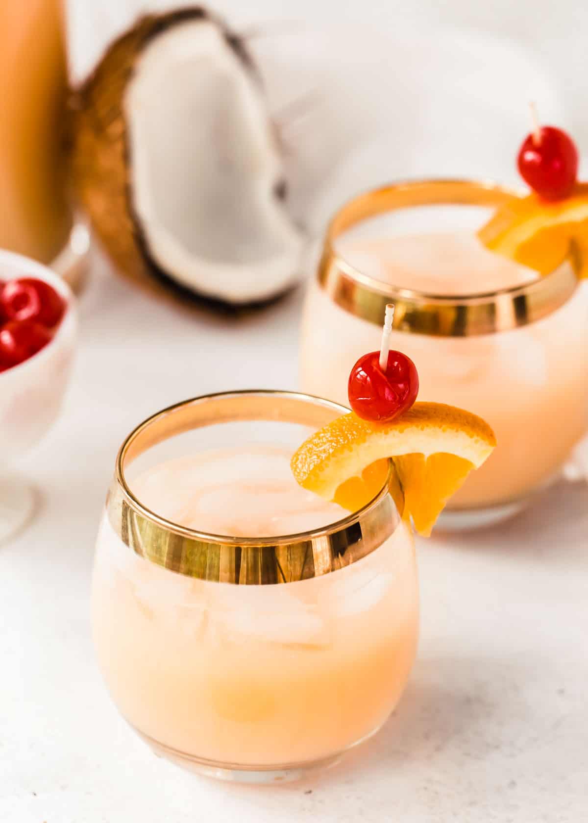 round glasses with orange punch garnished with orange slices and cherries.